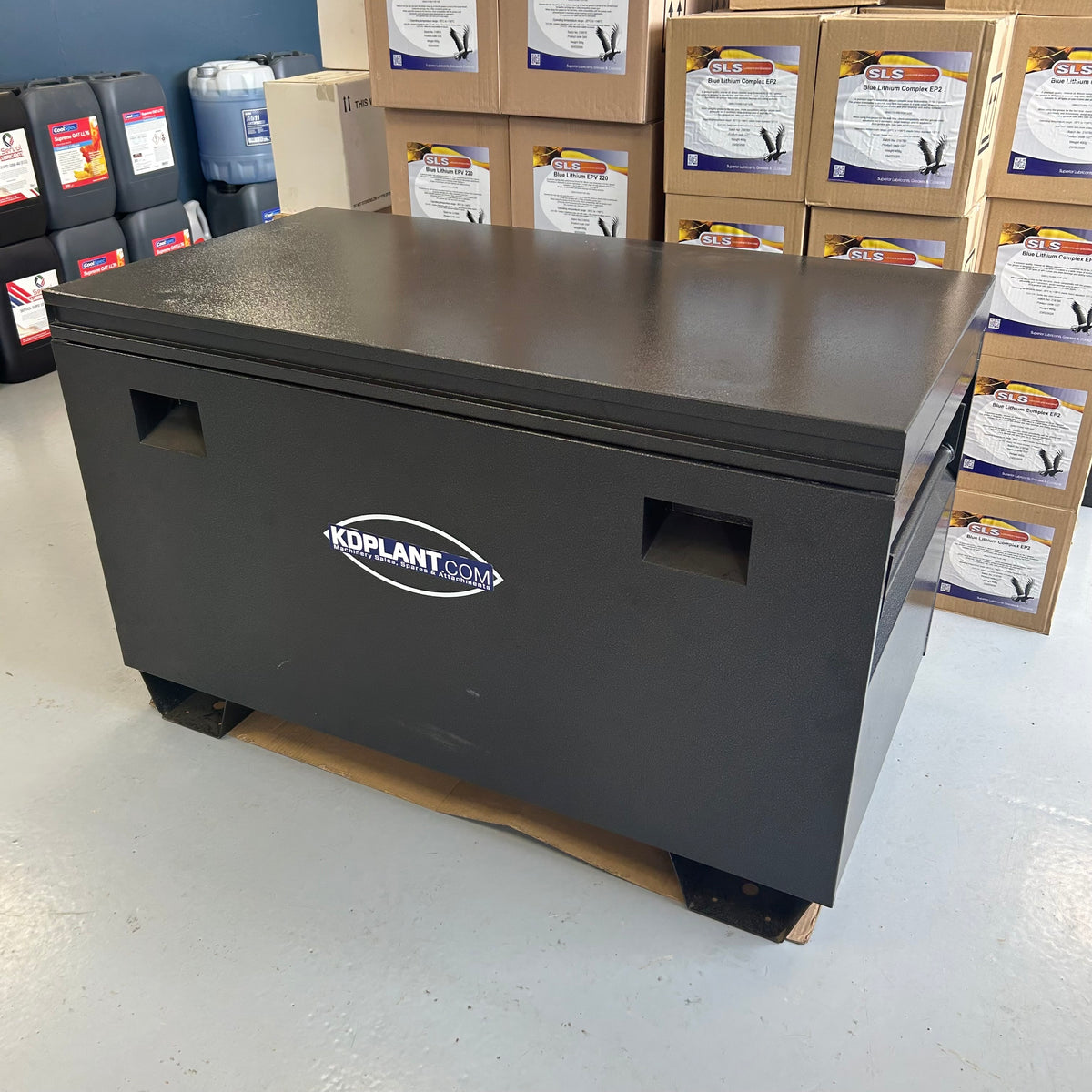 Black storage box with 'KDPlant.com' logo on a warehouse floor with boxes and containers in the background.