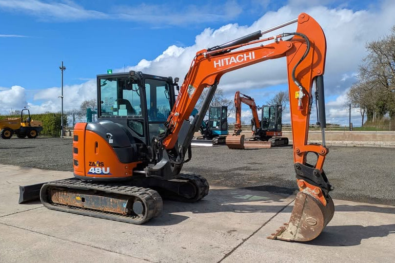 Orange Hitachi excavator on a concrete surface with a blue sky and trees in the background